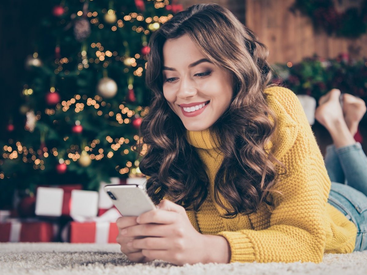 Frau mit iPhone vor einem Weihnachtsbaum