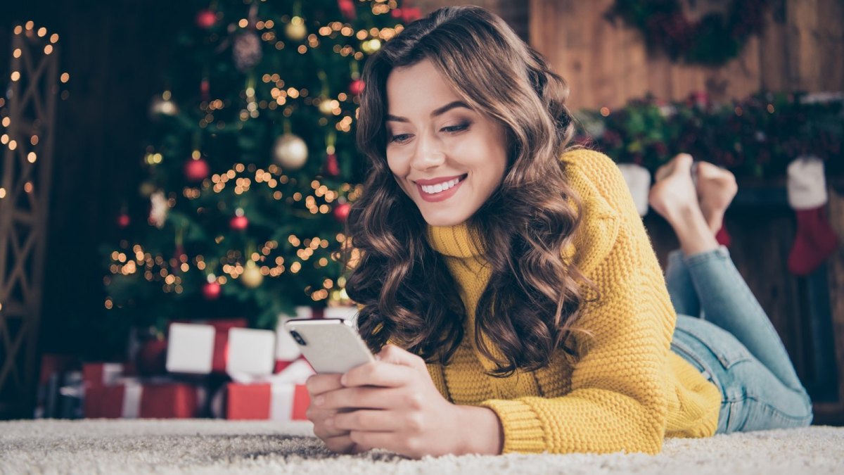 Frau mit iPhone vor einem Weihnachtsbaum