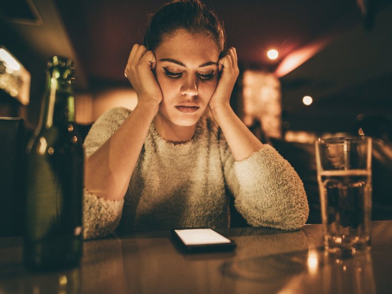 Frau schaut niedergeschlagen auf ihr Handy.