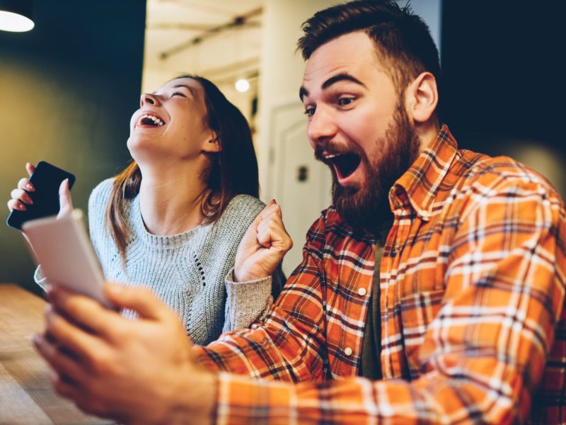 Mann und Frau schauen auf Handy und freuen sich sehr.