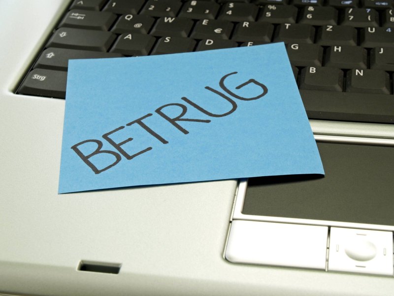 Auf einem Laptop liegt ein Zettel mit der Aufschrift "Betrug".