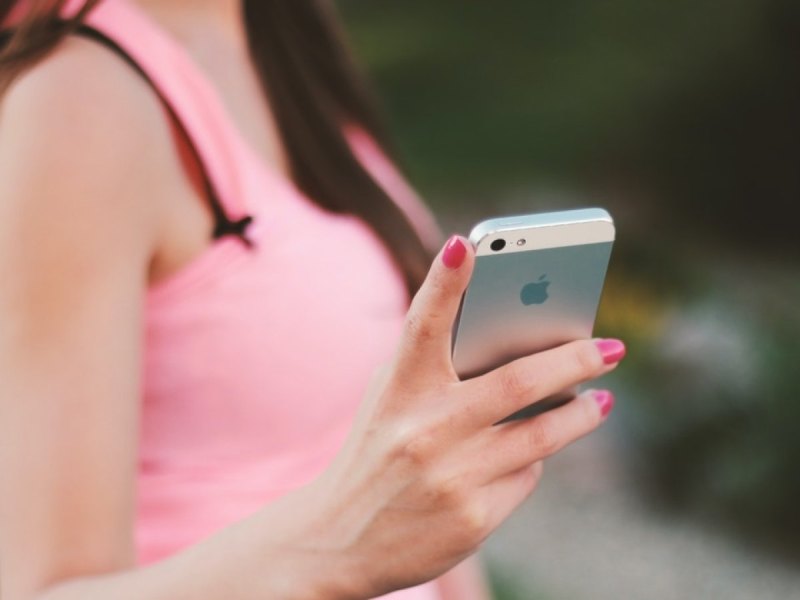 Eine Frau in einem rosafarbenen Shirt hat ein IPhone in der Hand.