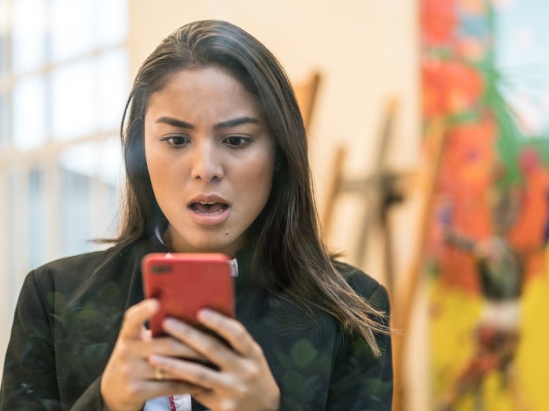 Frau blickt schockiert auf ihr iPhone