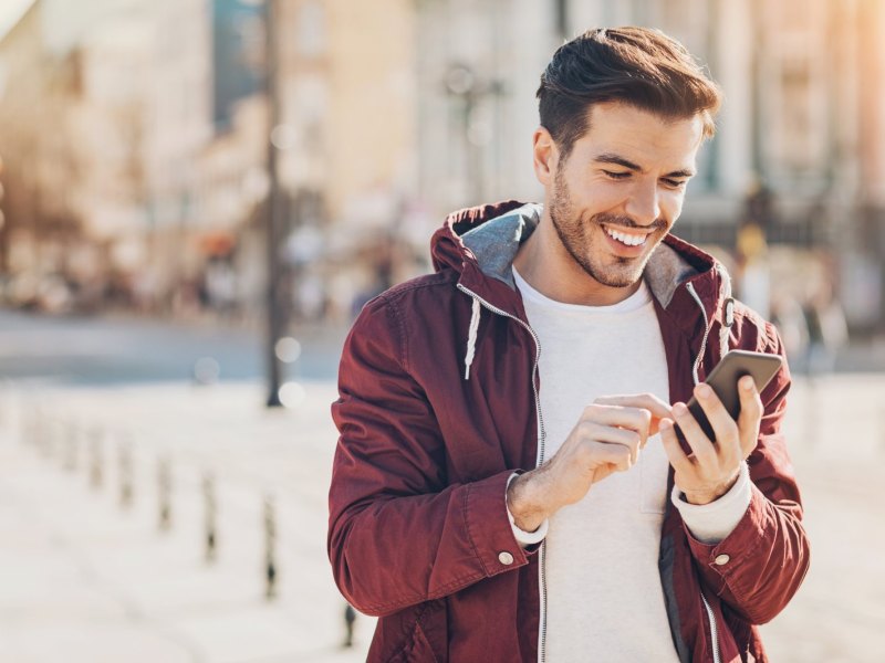 Mann hält Handy mit einem Lächeln im Gesicht in der Hand und blickt darauf.