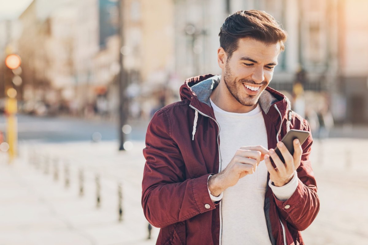 Mann hält Handy mit einem Lächeln im Gesicht in der Hand und blickt darauf.