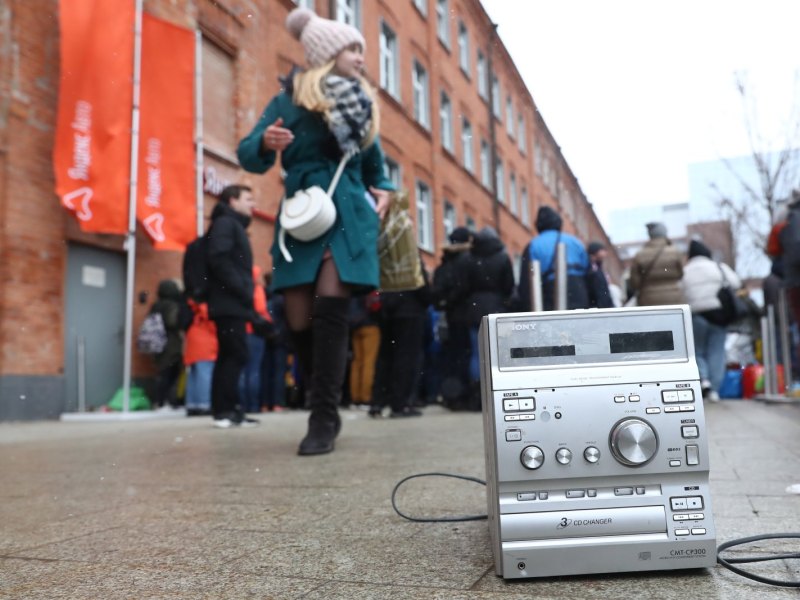 CD-Player steht auf Straßenboden vor Menschen.