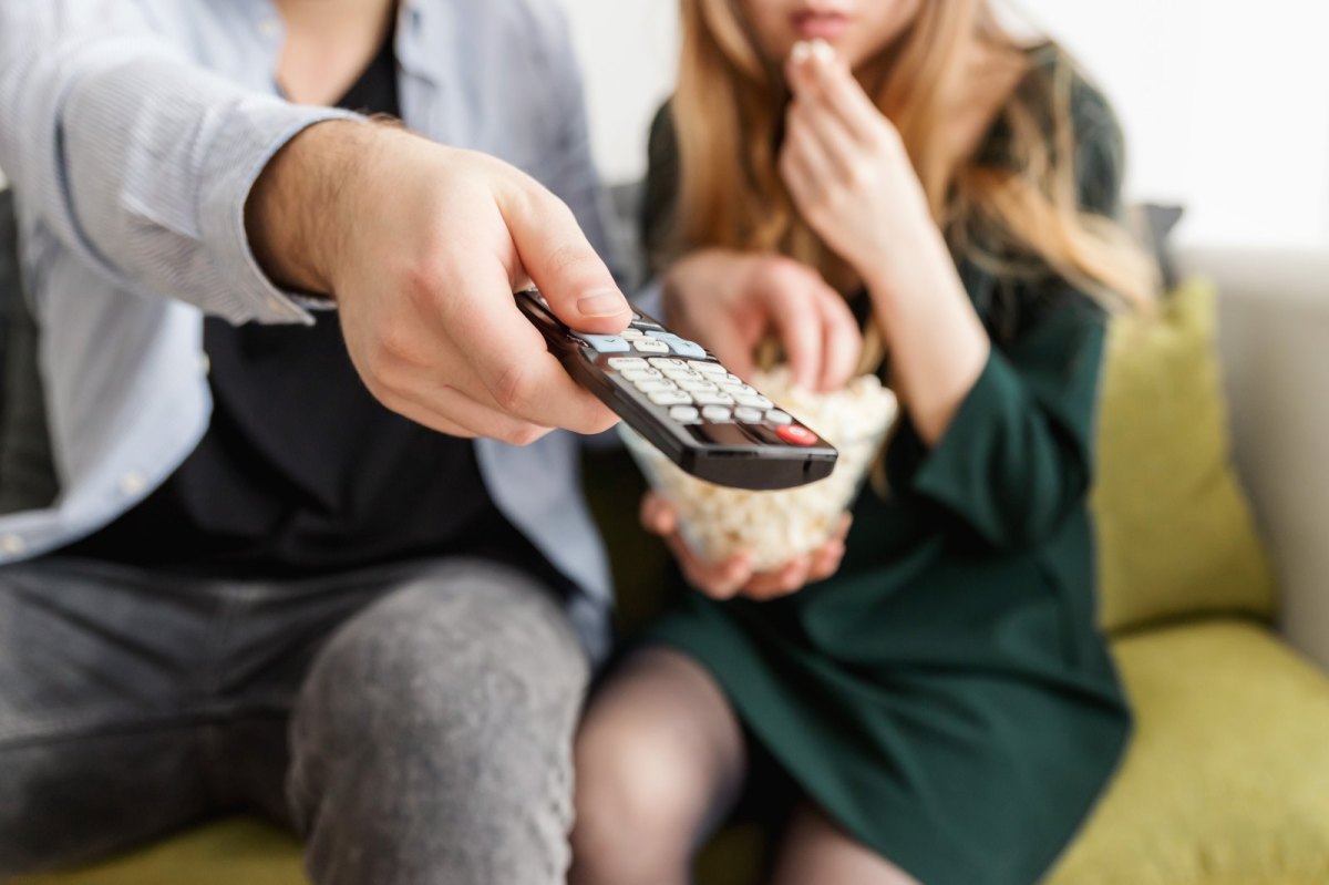 Paar sitzt mit Popcorn und Fernbedienung vor dem Fernseher