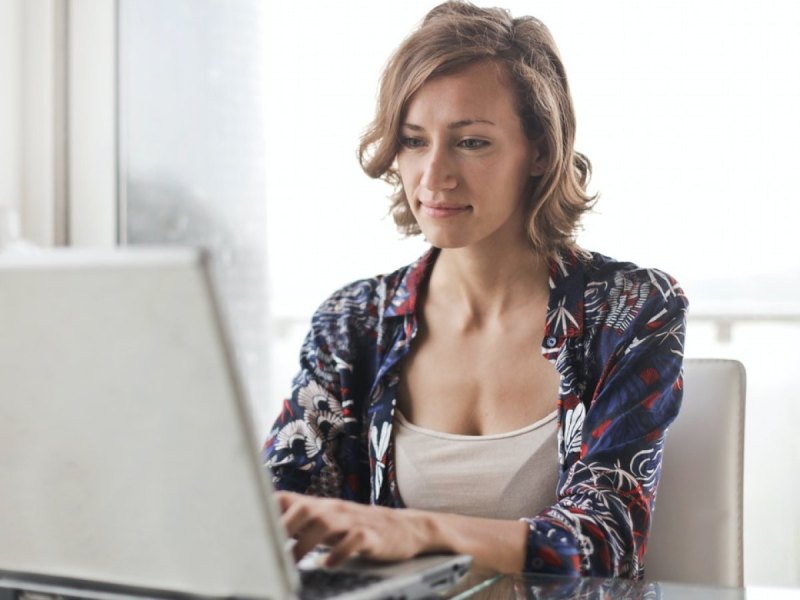 Eine Frau sitzt ein einem Tisch vor einem aufgeklappten Laptop.