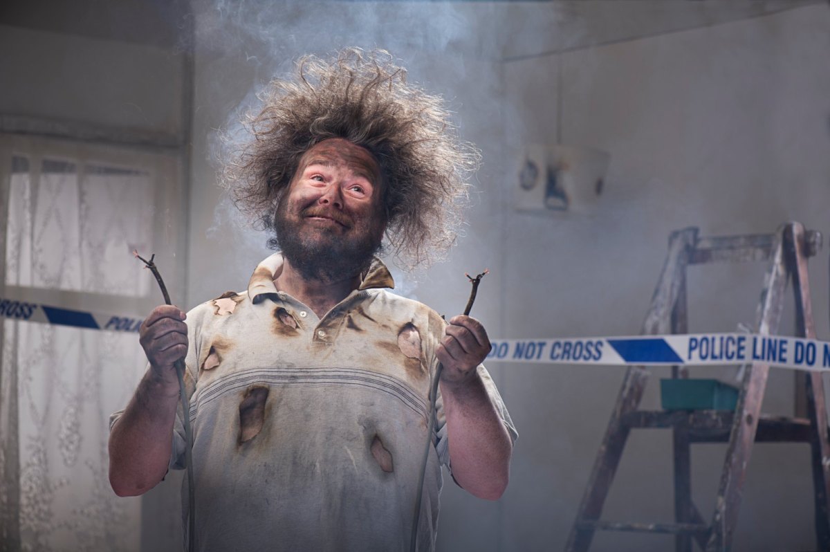 Mann mit abstehenden Haaren und rußbefleckt hält zwei verkohlte Kabel in der Hand.