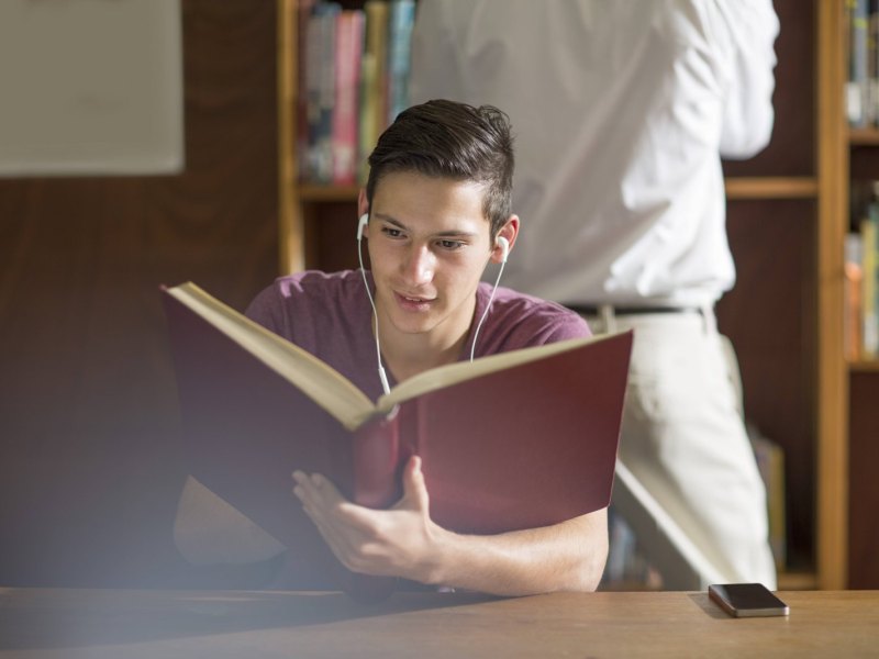 Junge hört Musik und liest ein Buch.