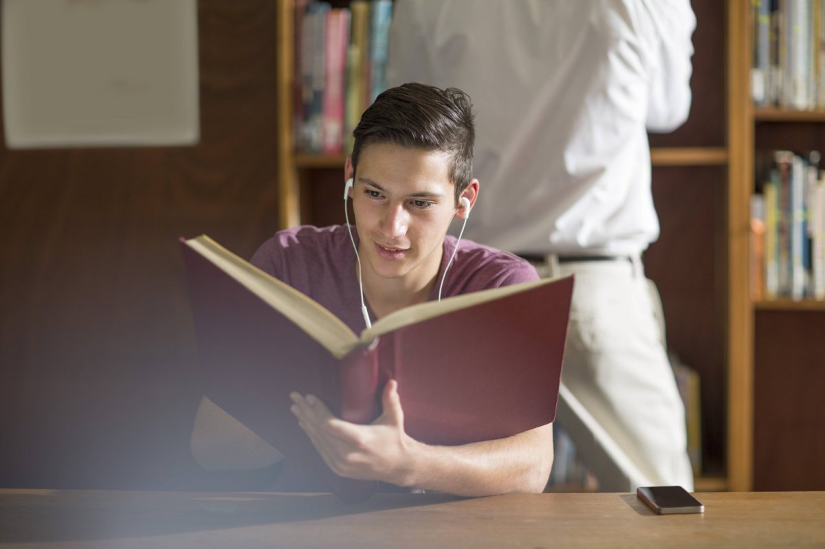 Junge hört Musik und liest ein Buch.