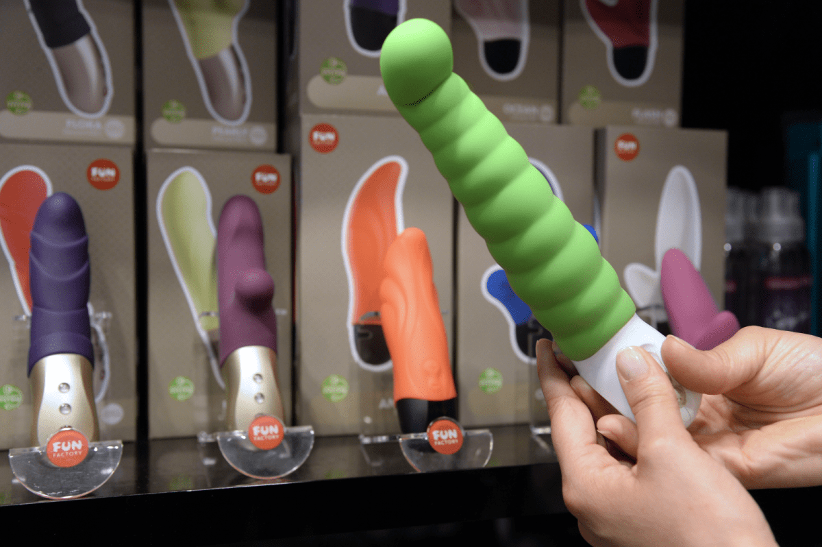 Hände halten grünen Vibrator in der Hand mit anderen Vibratoren im Hintergrund