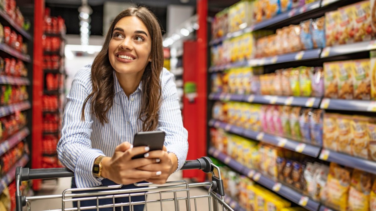 Frau mit Handy am Einkaufswagen