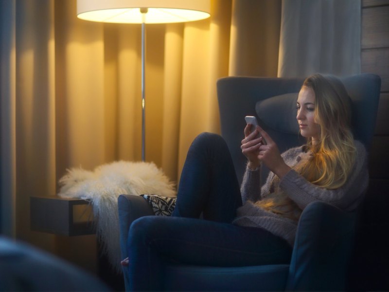 Frau sitzt auf dem Sofa mit einem Handy in der Hand.