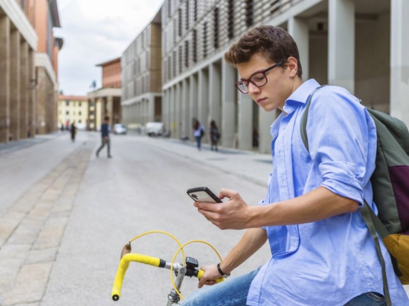 Ein Mann auf einem Fahrrad hält ein Smartphone in der Hand.