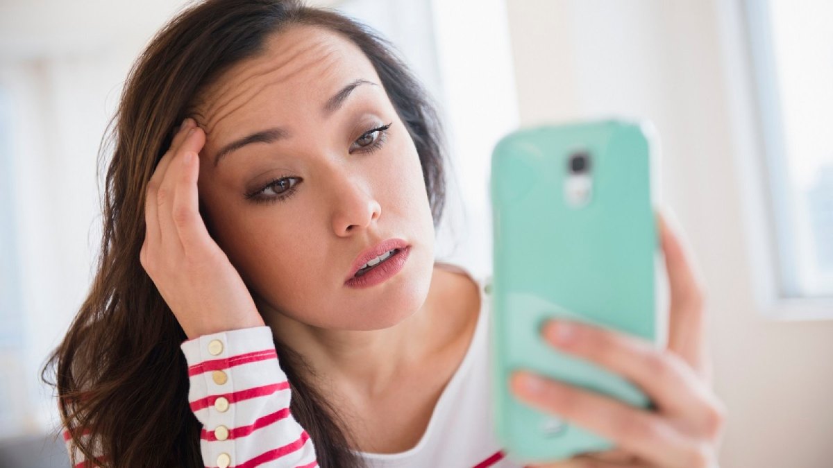 Frau schaut genervt/böse auf ihr Handy.