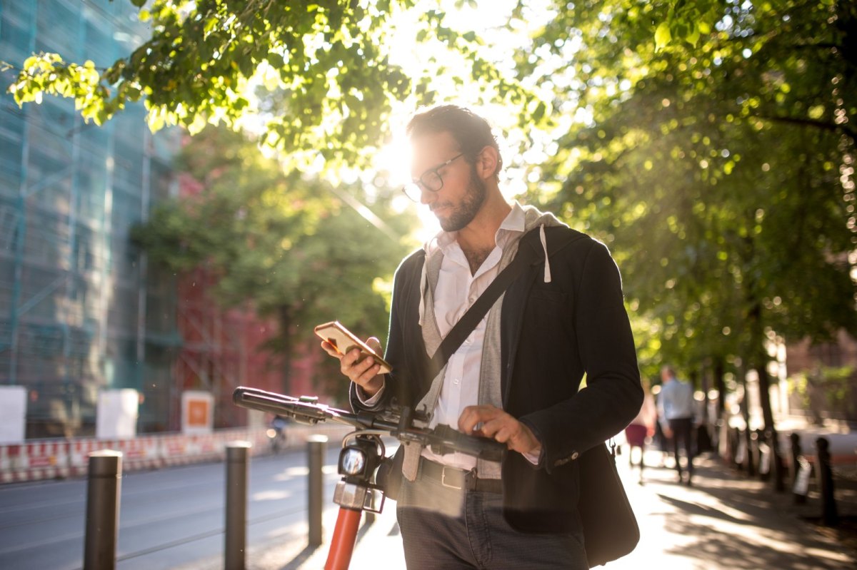 Mann blickt auf sein Handy und läuft währenddessen draußen mit seinem Fahrrad.