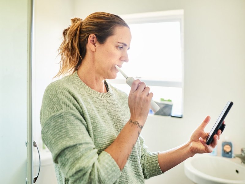 Frau putzt Zähne und hat Handy in der Hand.