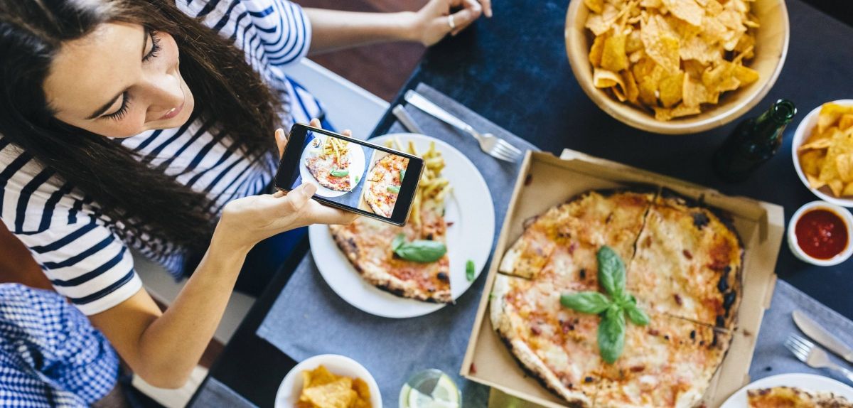 Frau fotografiert ihre Pizza auf dem Tisch.