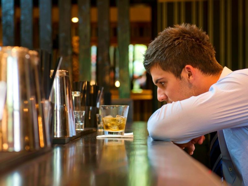 Mann sitzt alleine in einer Bar vor einem alkoholischen Getränk.