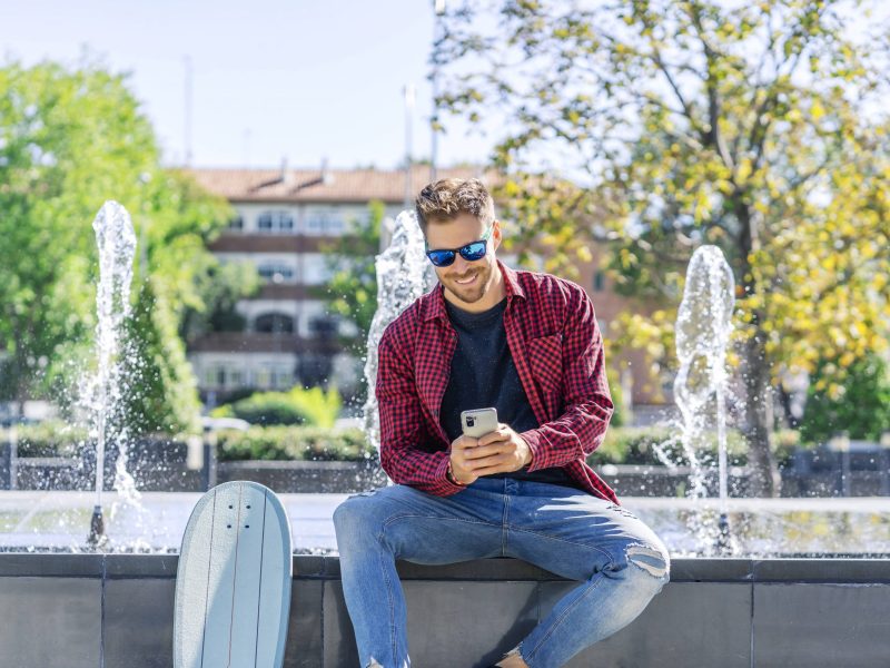 Mann sitzt im Park mit dem Handy in der Hand.