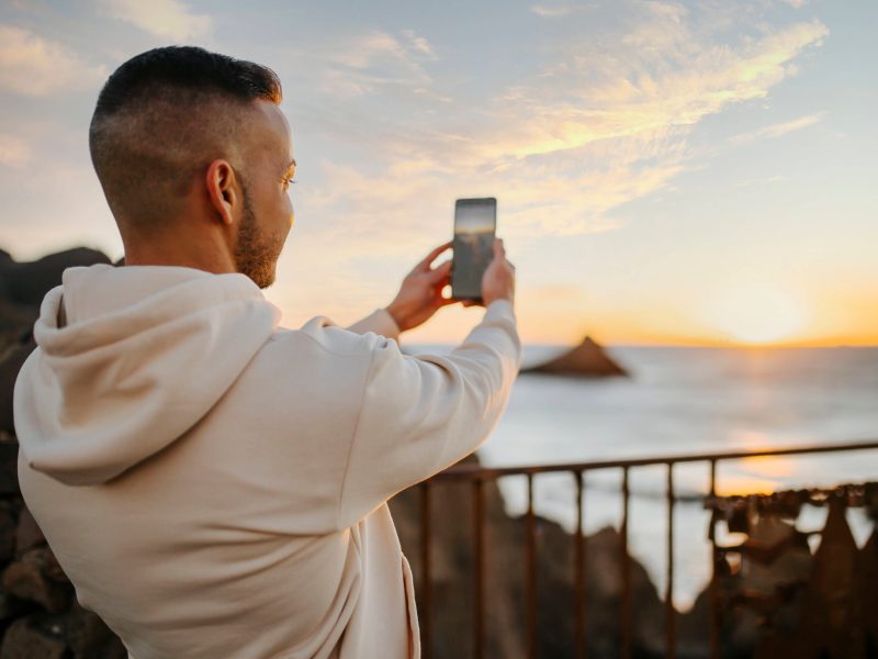 Mann nimmt Bild von Sonnenuntergang mit Handy auf