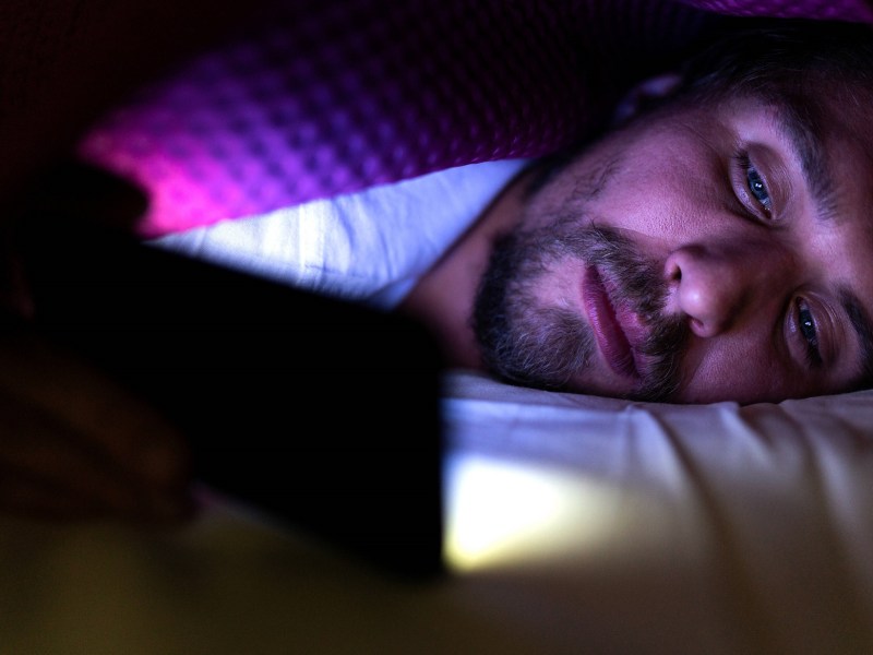 Mann liegt mit Smartphone im Bett