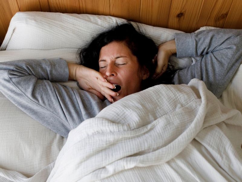 Frau liegt im Bett und gähnt.