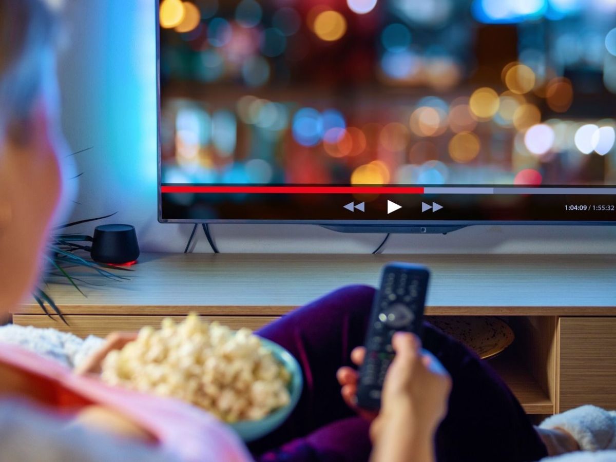 Frau sitzt vor dem Fernseher mit einer Schüssel Popcorn und streamt.