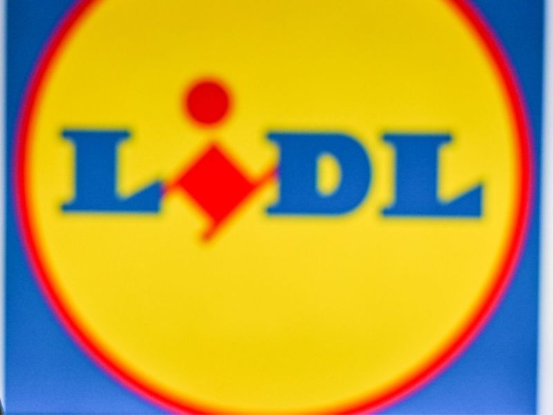 Frau vor Lidl-Logo schaut auf ihr Handy