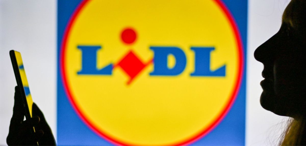 Frau vor Lidl-Logo schaut auf ihr Handy