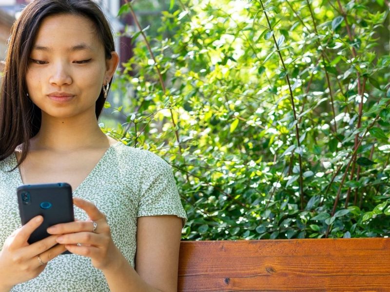 Frau sitzt mit Handy im Garten