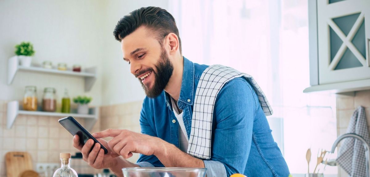 Mann mit Smartphone in der Küche