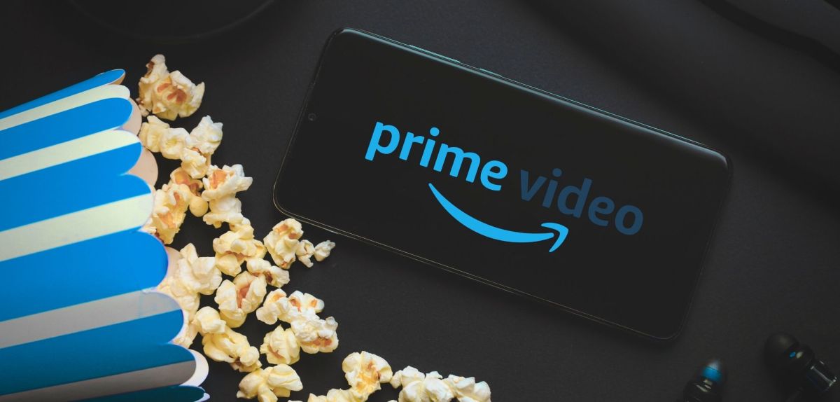 Logo von Amazon Prime Video auf einem Handy, daneben eine Tüte Popcorn.