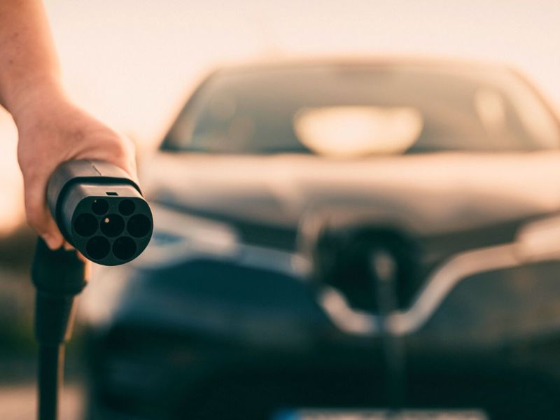 Person mit Ladestecker eines Elektroautos in der Hand