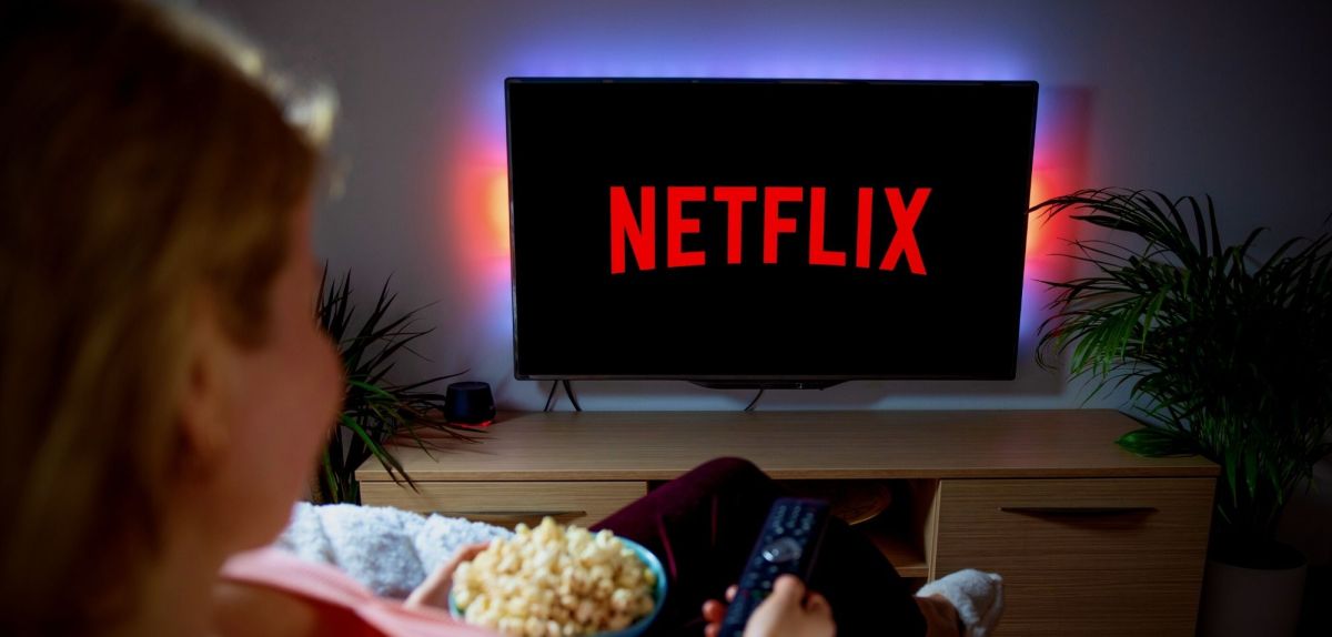 Frau sitzt mit einer Schüssel Popcorn vor dem TV und schaut Netflix.