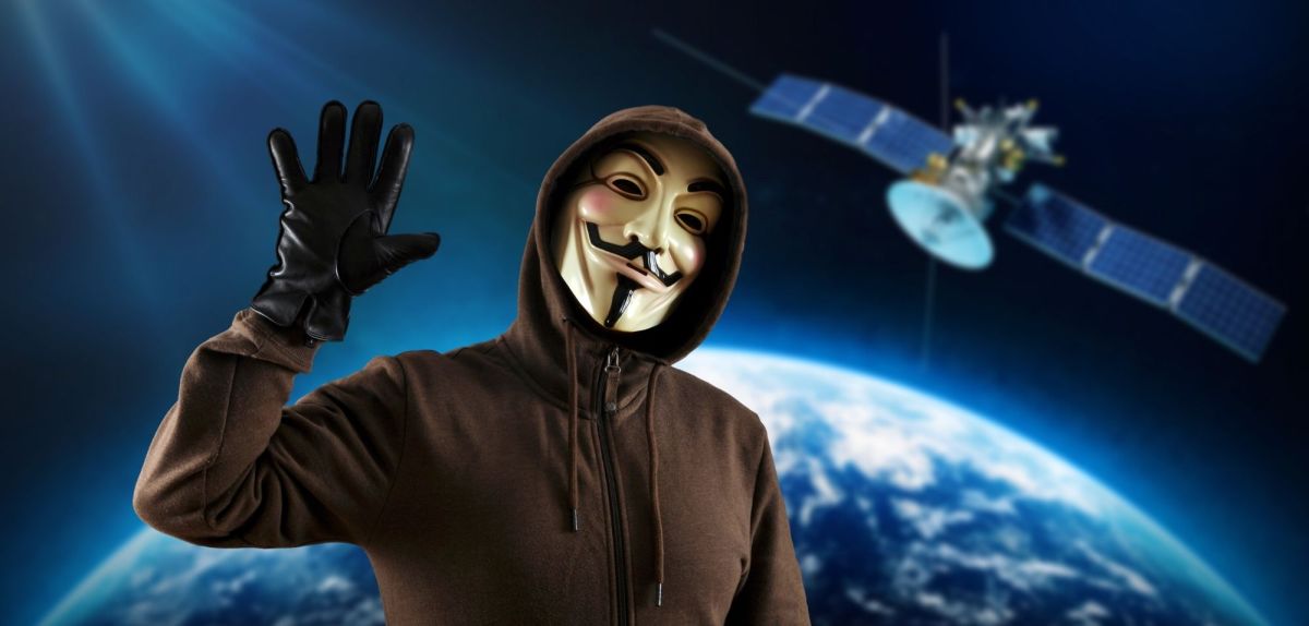 Person mit Guy Fawkes-Maske vor einem Satelliten