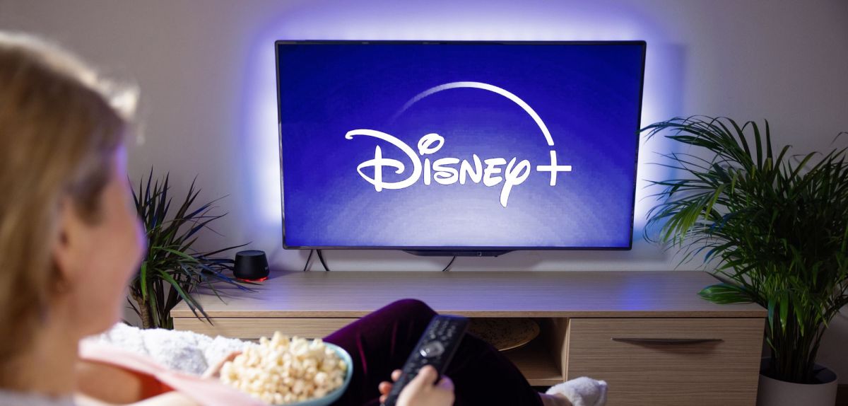 Disney Plus-Logo auf einem TV, davor eine Frau mit Popcorn.