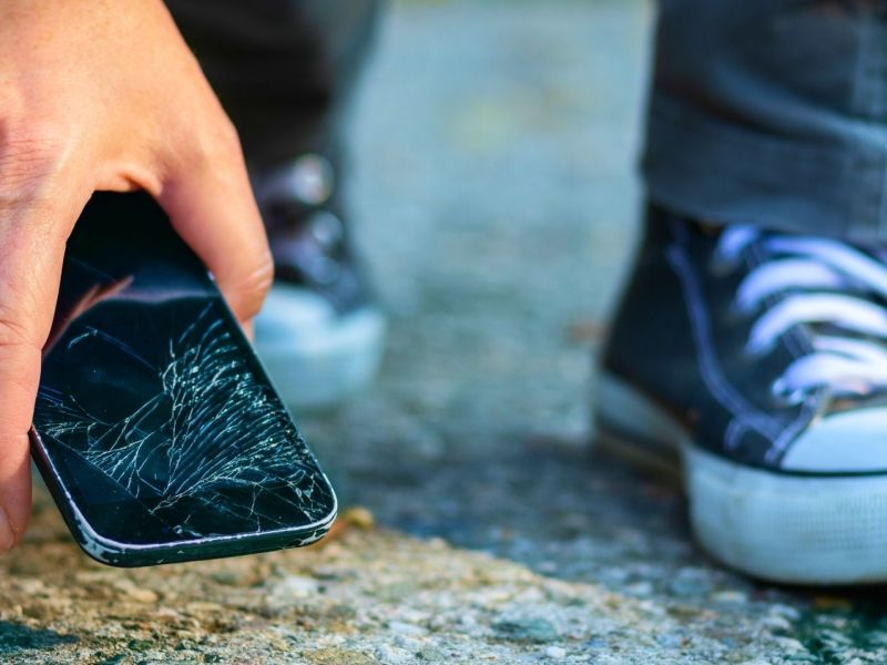 Person hebt kaputtes Smartphone vom Boden auf