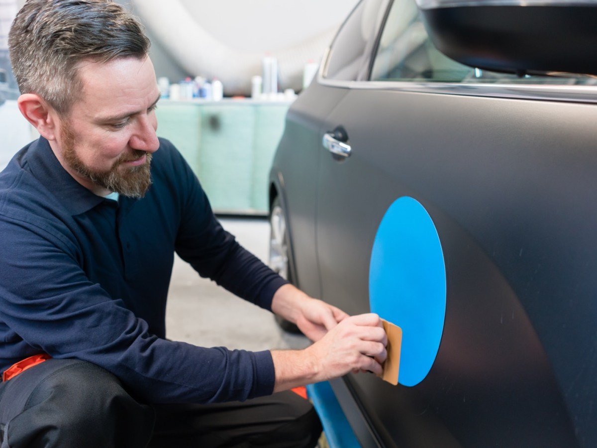 Mann bringt Aufkleber am Auto an