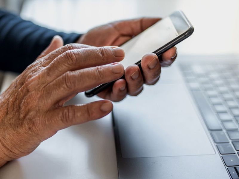 Alte Person nutzt ein Smartphone vor einem Handy.