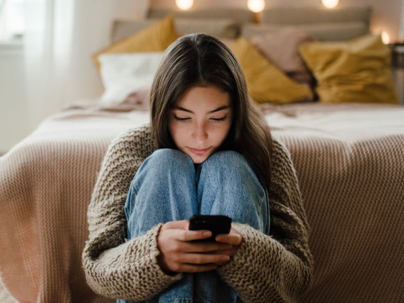 MÃ¤dchen sitzt Zuhause auf dem Boden an ihrem Handy.