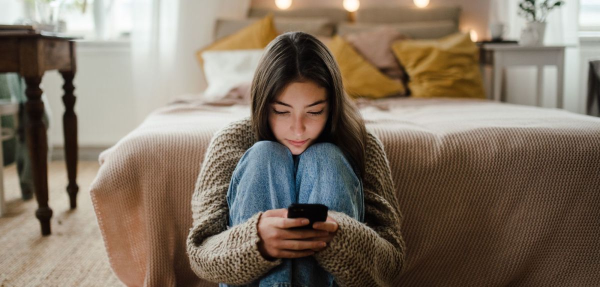 MÃ¤dchen sitzt Zuhause auf dem Boden an ihrem Handy.