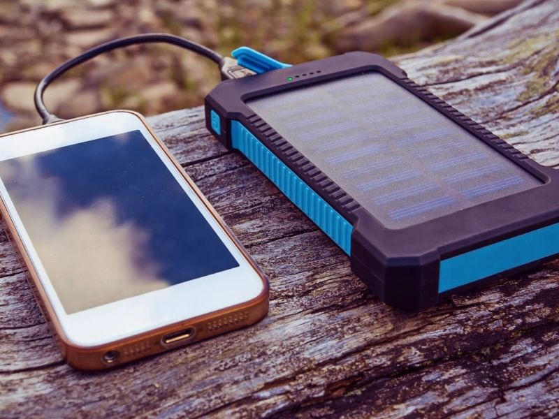 Solar-Powerbank mit Smartphone auf Baumstamm.