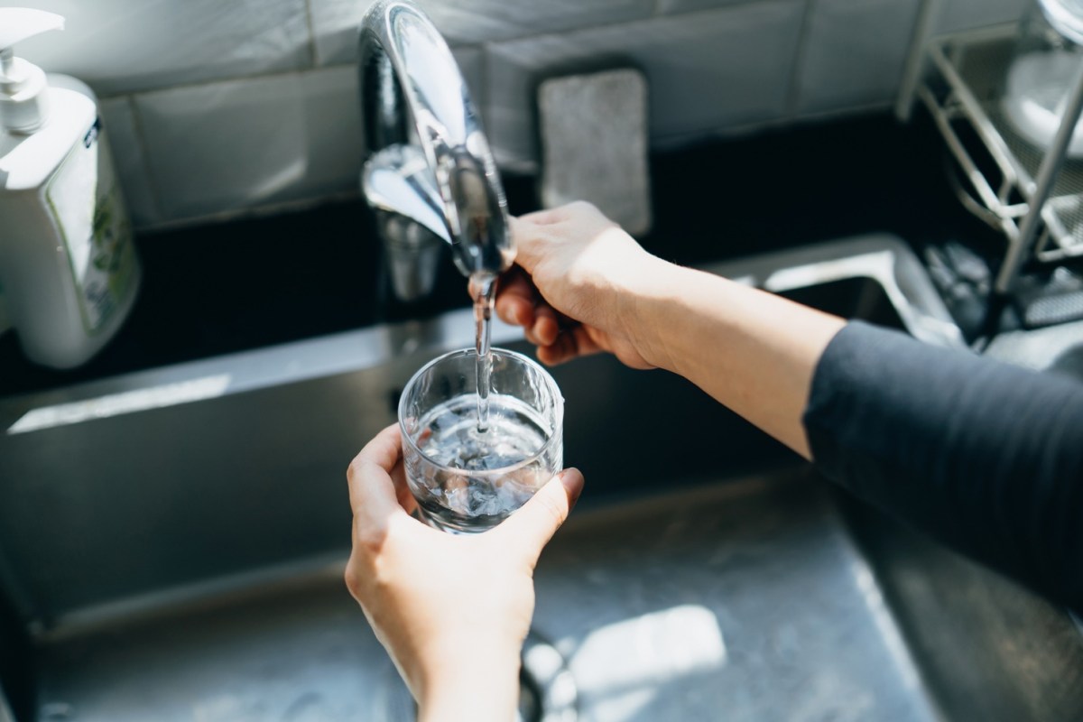 Frau gießt Wasser aus dem Hahn in ein Glas