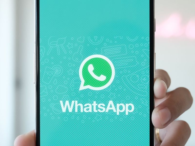 Person hält Handy mit WhatsApp-Logo in die Kamera.