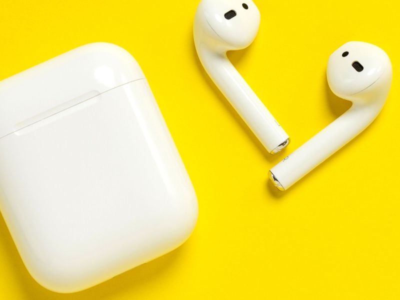 AirPods mit Ladeschatulle auf gelbem Untergrund.