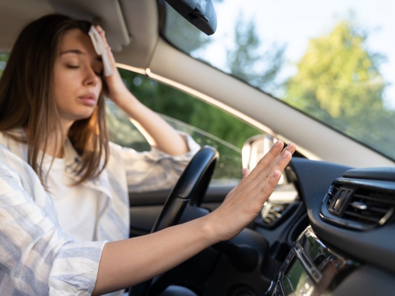 Frau hält im Auto die Hand vor die Klimaanlage