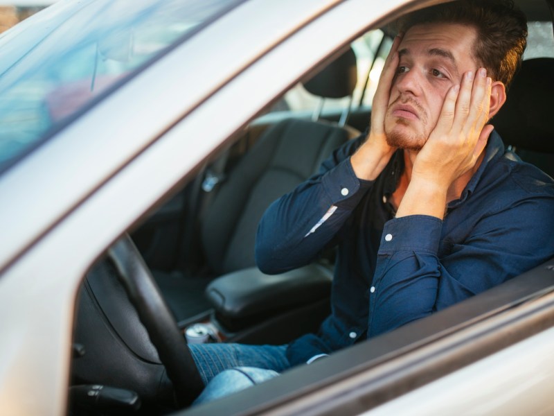 Mann im Stau im Auto hält sich aus Frust das Gesicht