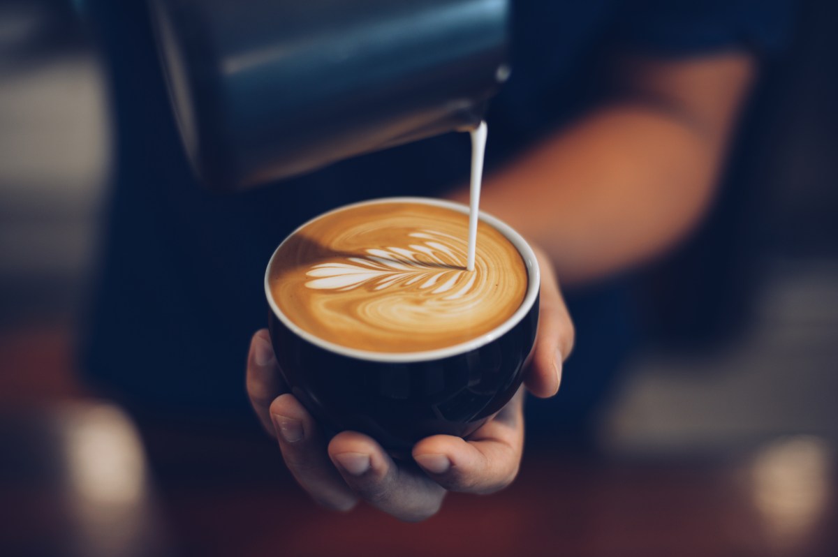 Milch wird in eine Tasse Kaffee gegossen.